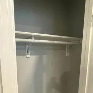 Empty closet with a rod and shelf. White brackets, gray walls, white door frame.