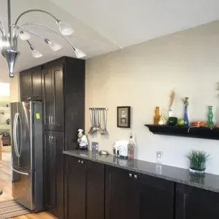 Kitchen with dark cabinets, stainless steel refrigerator, and decorative shelf with objects.