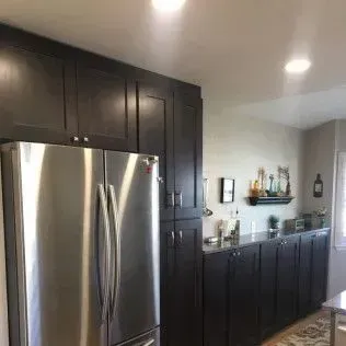 Stainless steel refrigerator next to dark wood cabinets in a kitchen.