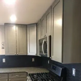 Gray kitchen cabinets with stainless steel microwave above a stove.