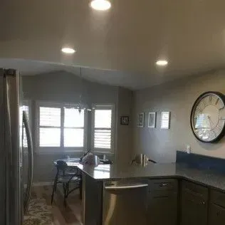 Kitchen with a stainless steel refrigerator, island with a sink, and a dining table by a window.