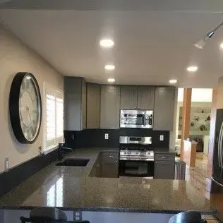 Kitchen with gray cabinets, a granite countertop, and a large black clock.