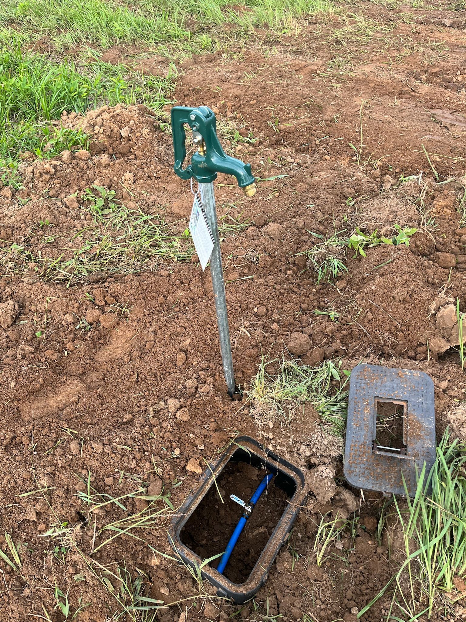 A faucet is sitting in the dirt next to a box of water.