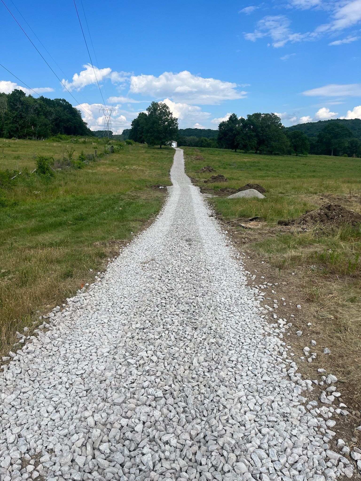 A gravel road going through a grassy field on a sunny day.