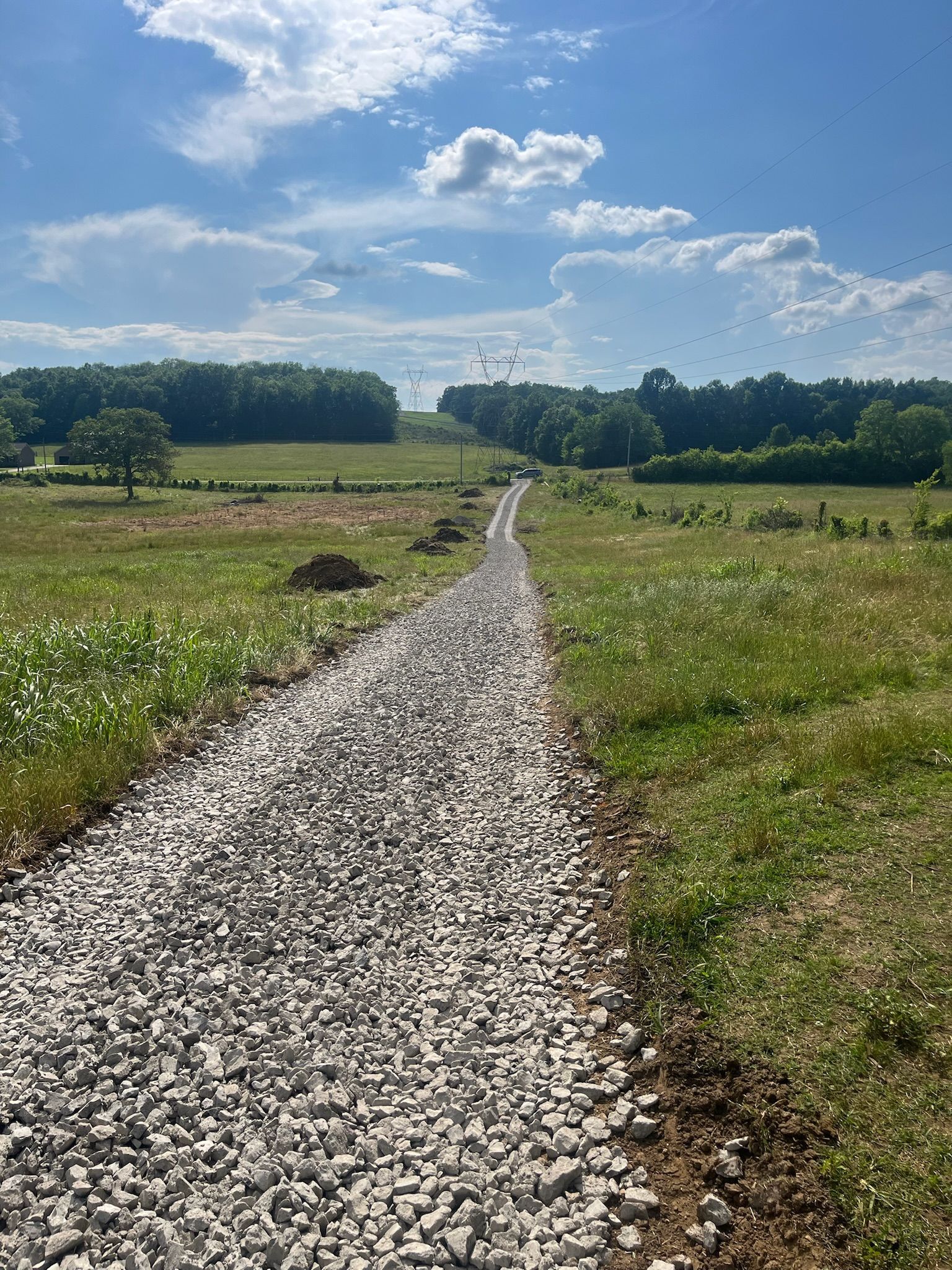 A gravel road going through a grassy field on a sunny day.