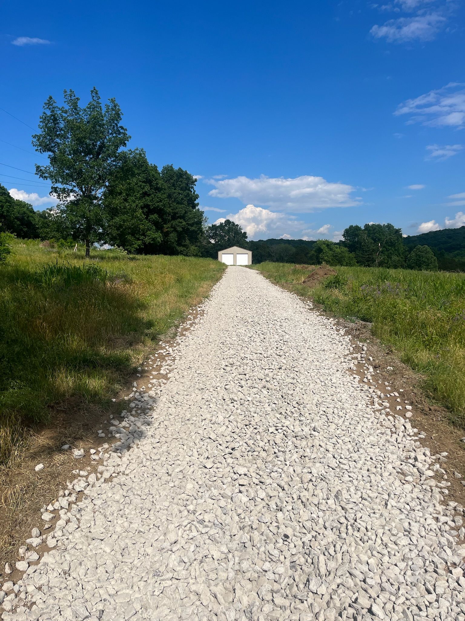 A gravel road leading to a house in the middle of a field.