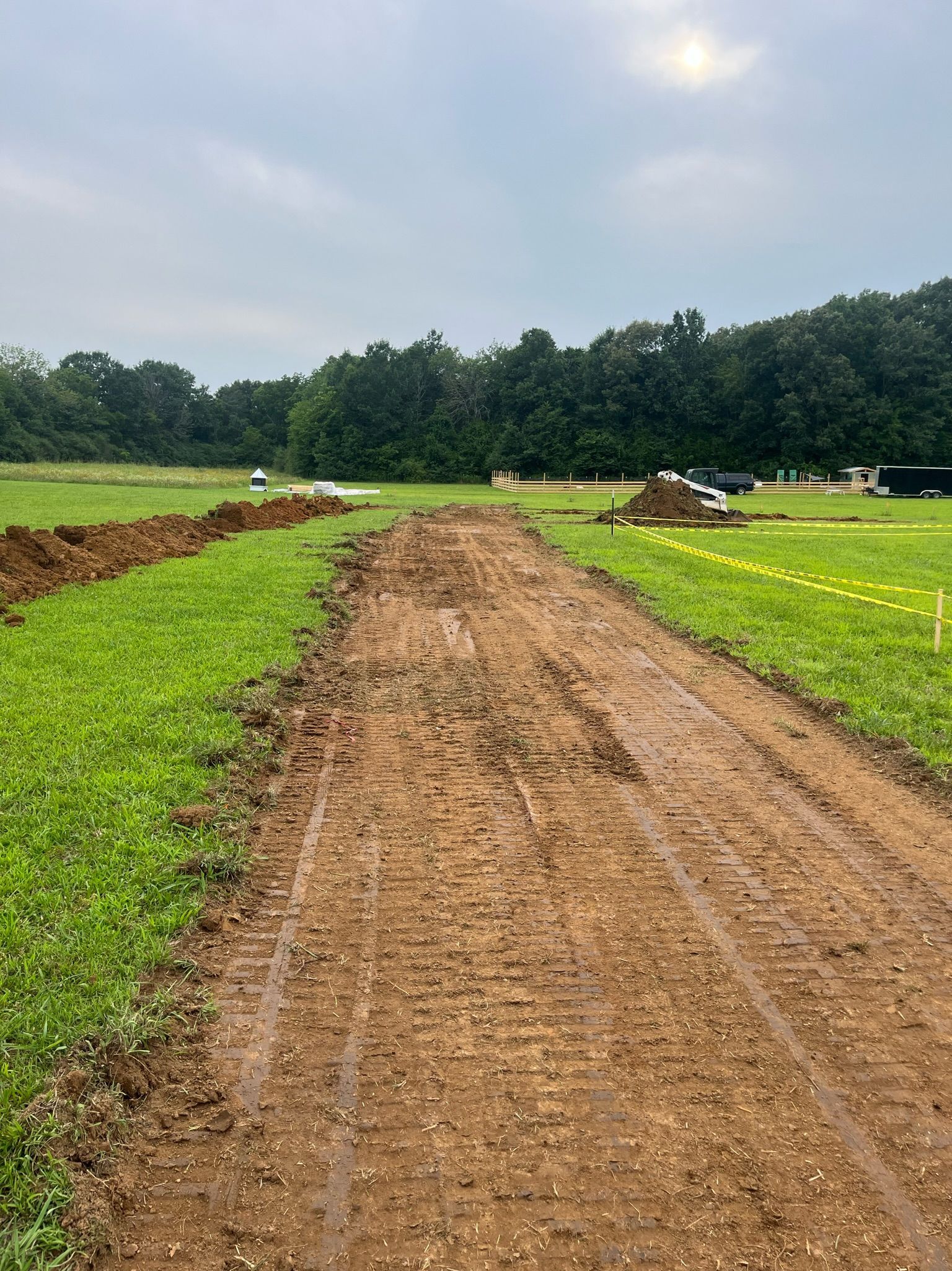 A dirt road going through a green field.