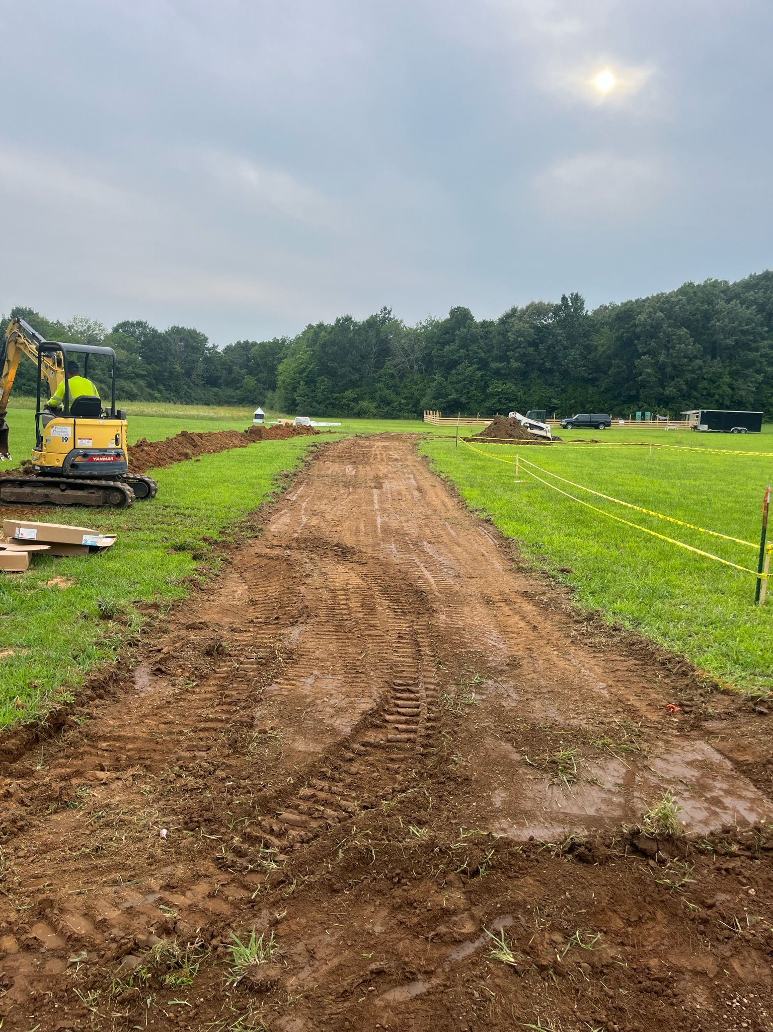 A yellow excavator is working on a dirt road in a field.