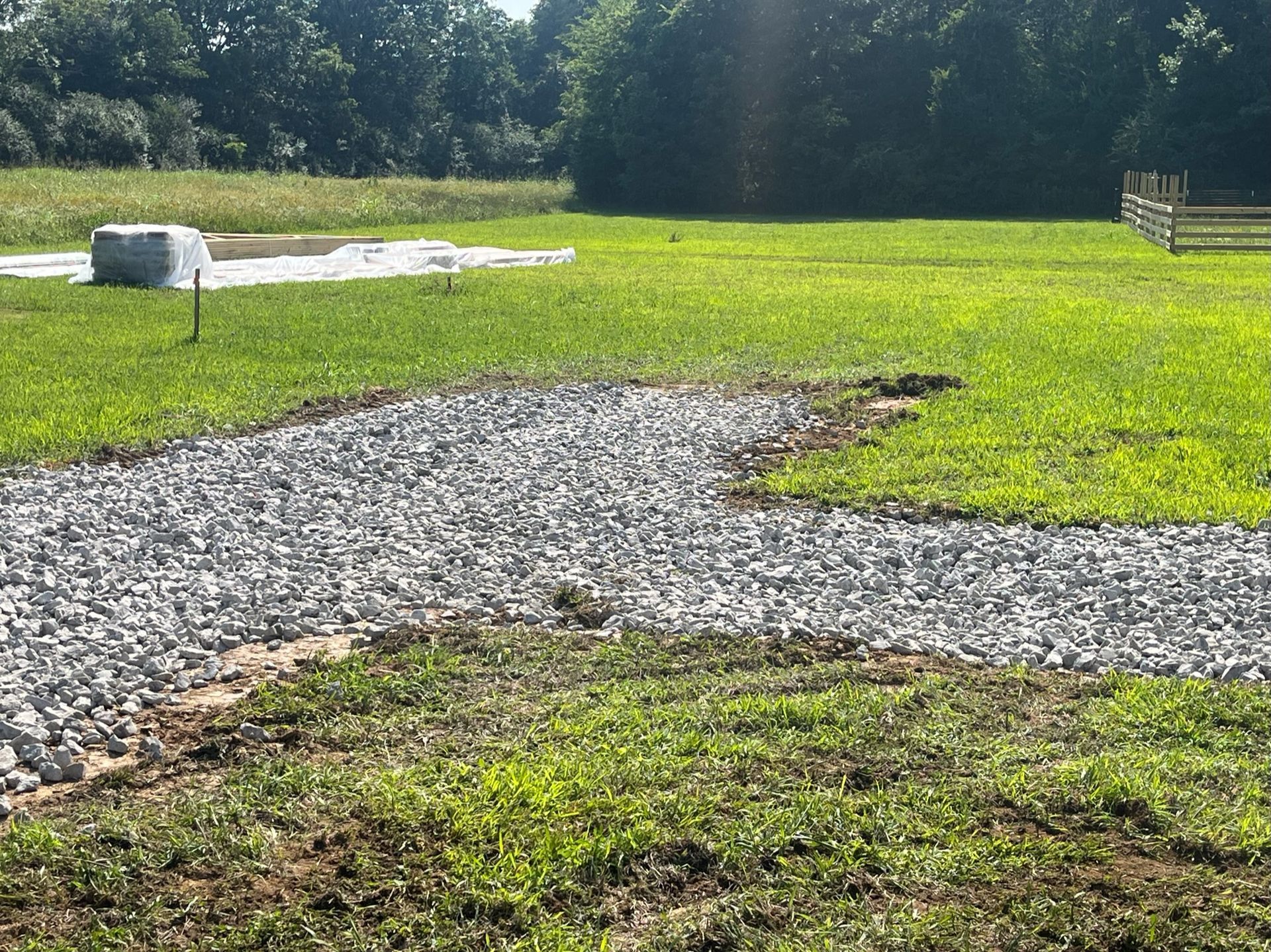 A gravel road going through a grassy field with trees in the background