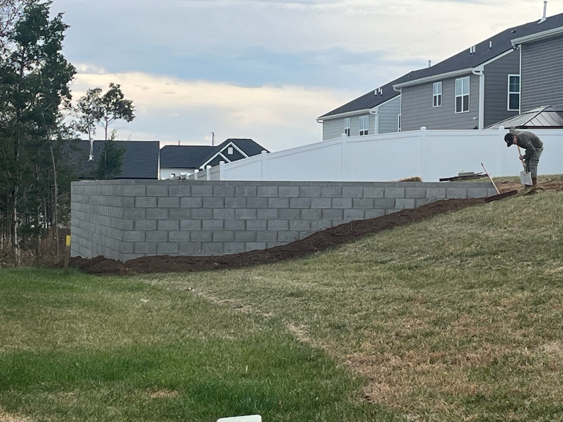 A man is standing on top of a grassy hill next to a brick wall.