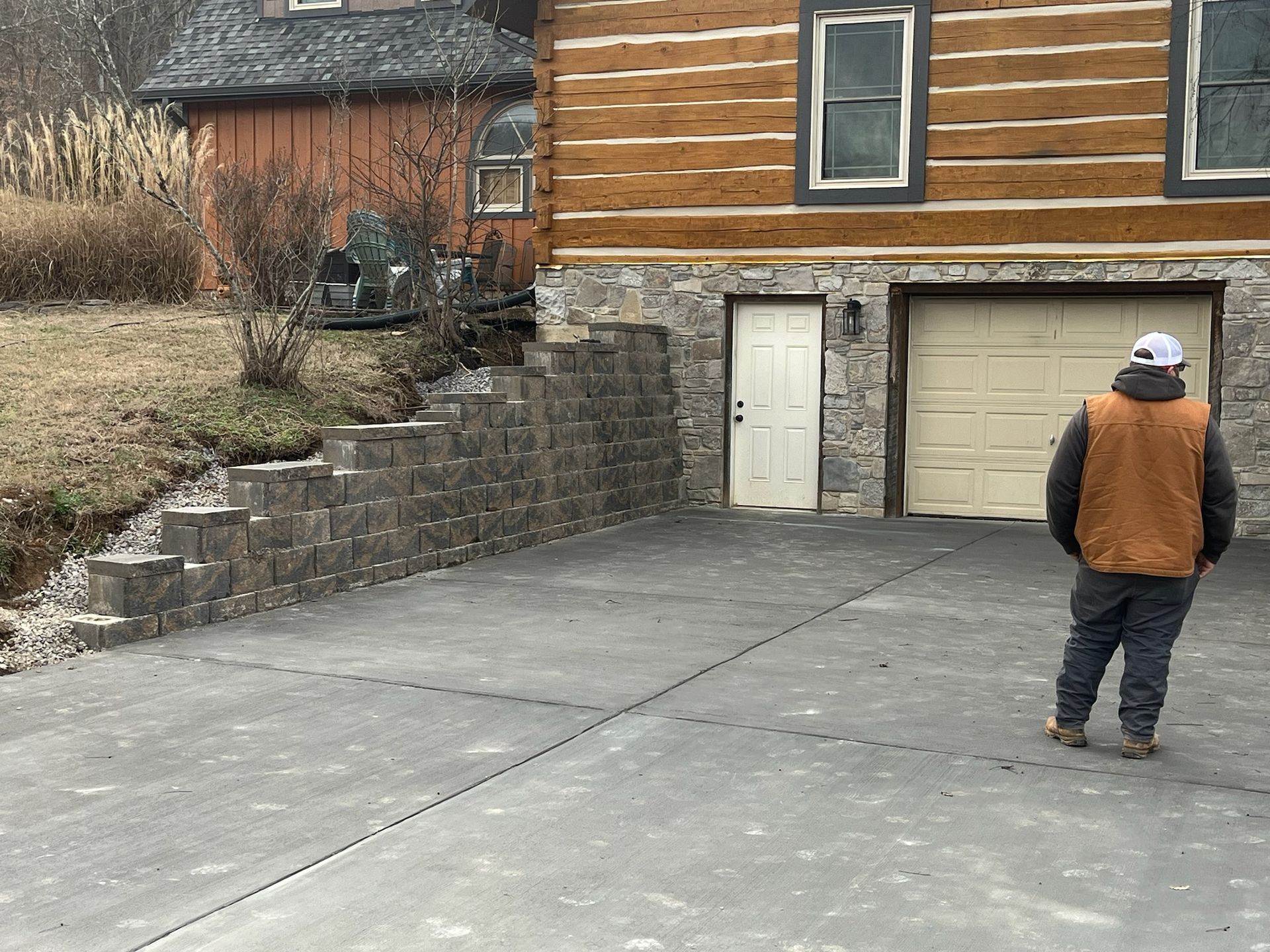 A man is standing in a driveway in front of a log cabin.