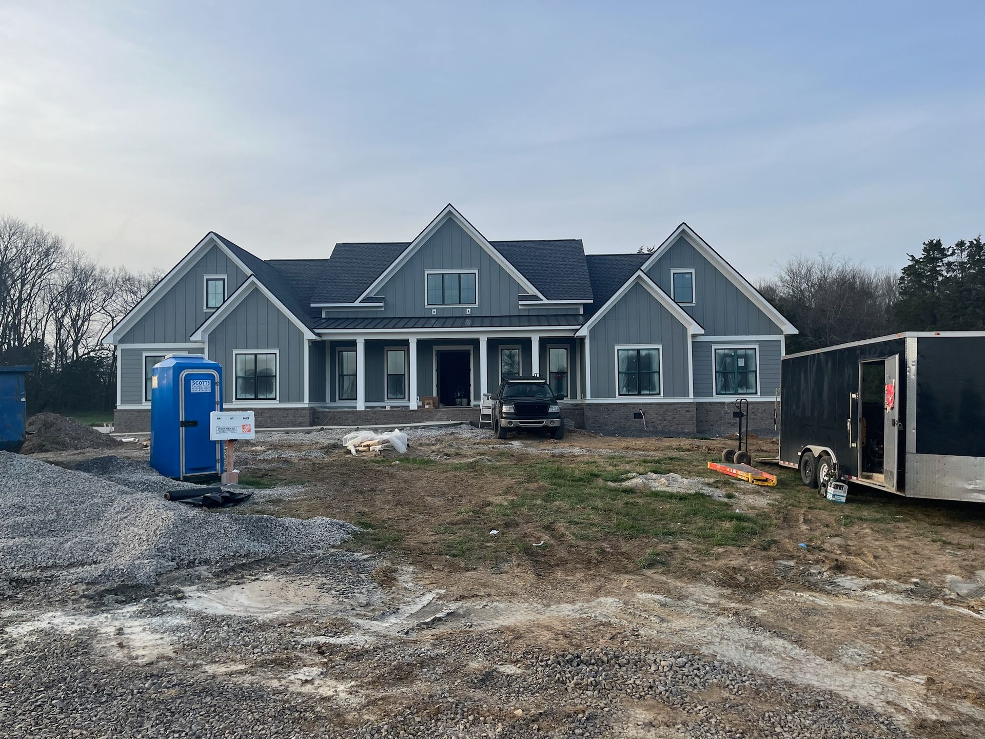 A large house under construction with a blue portable toilet in front of it.