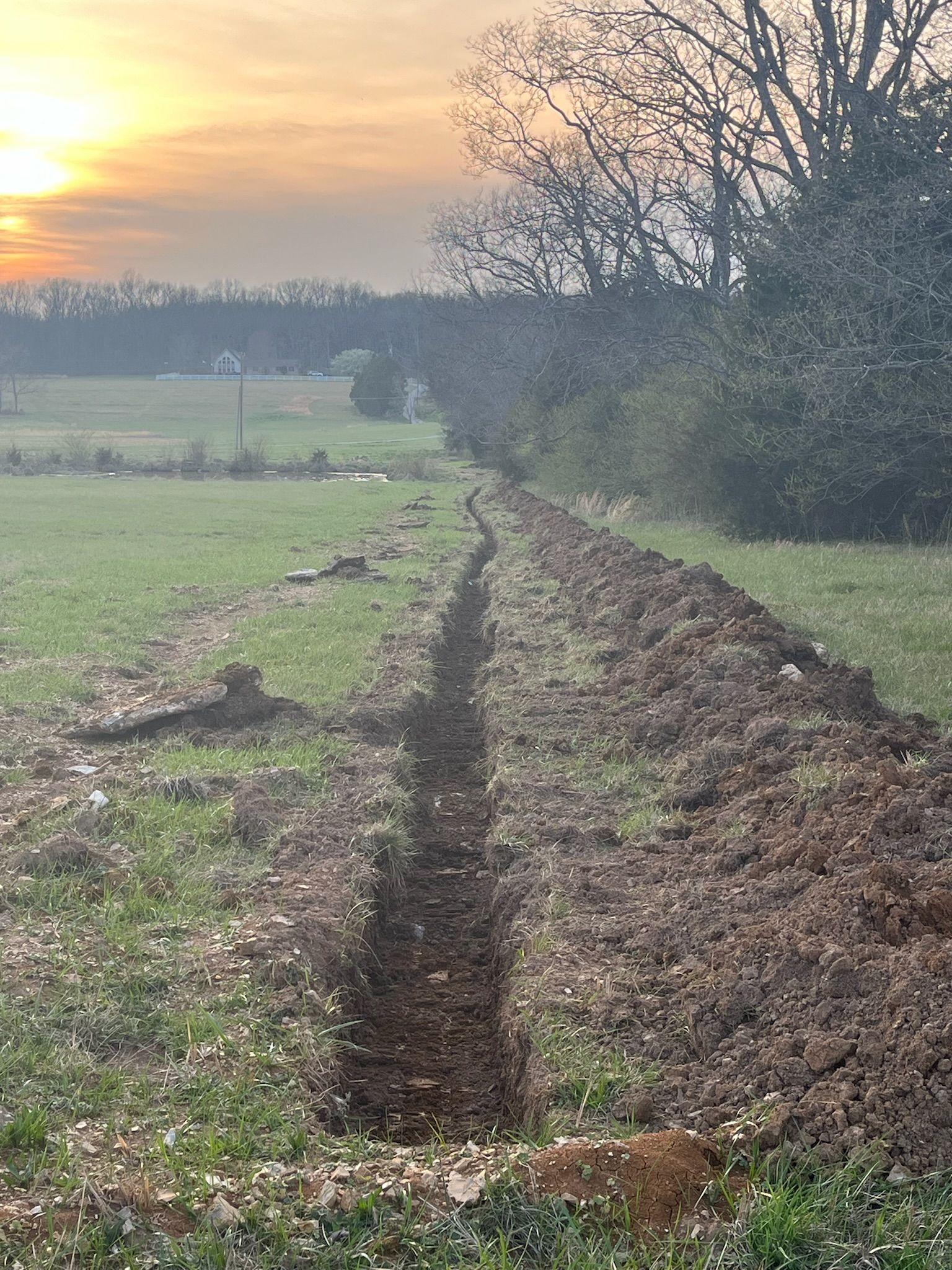A dirt road in a field with a sunset in the background.