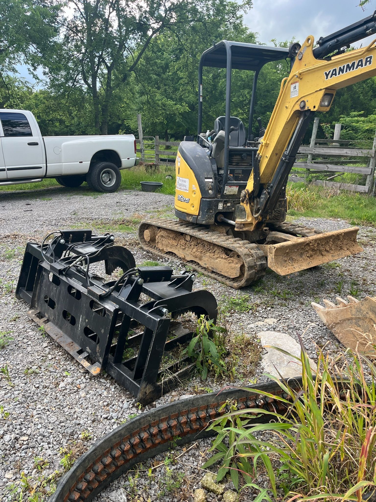 A yellow excavator is parked in a gravel lot next to a white truck.