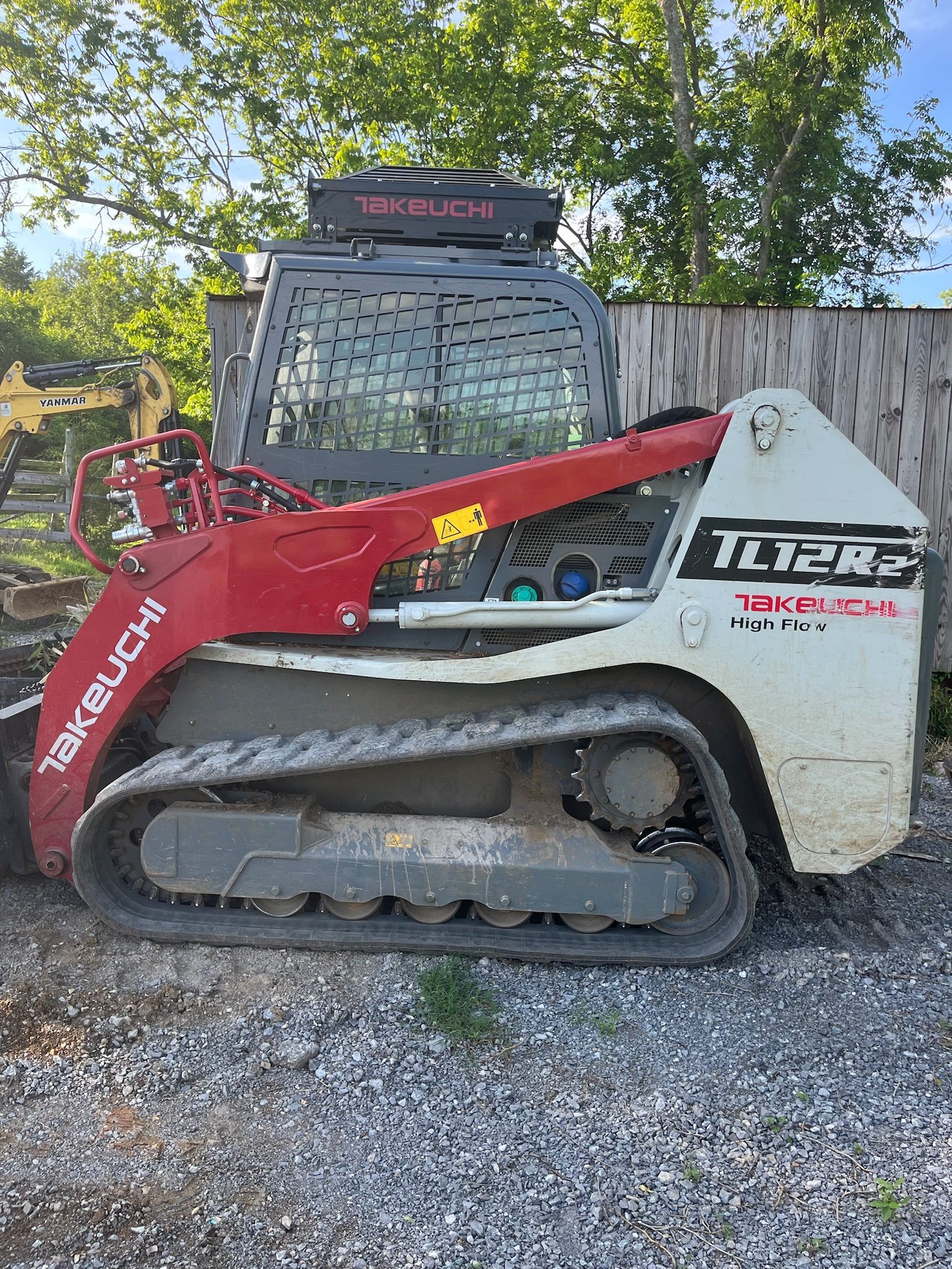 A skid steer is parked in a gravel lot next to a fence.
