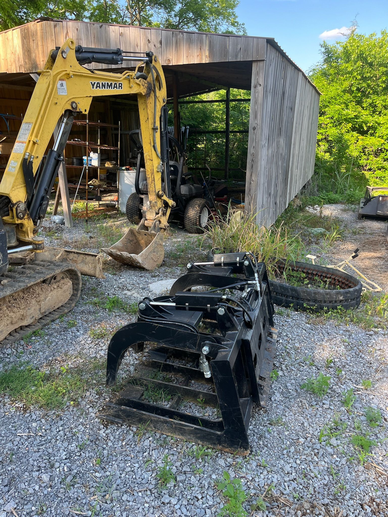 A yellow excavator is parked in front of a shed.