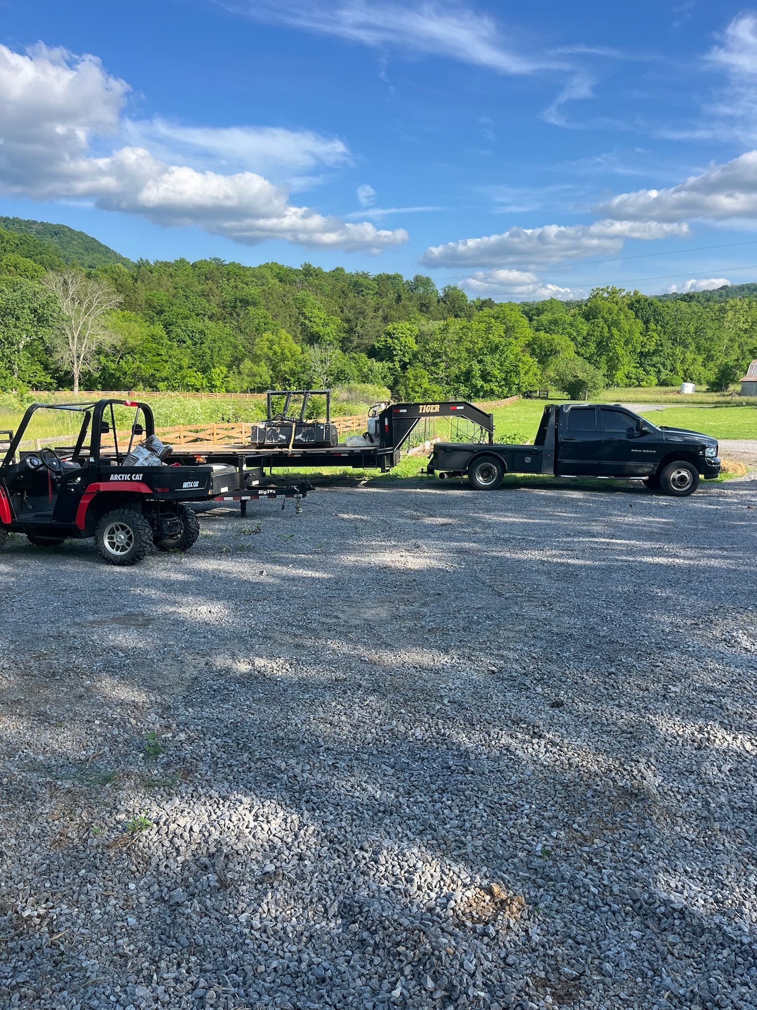 A truck is towing a atv in a gravel lot.