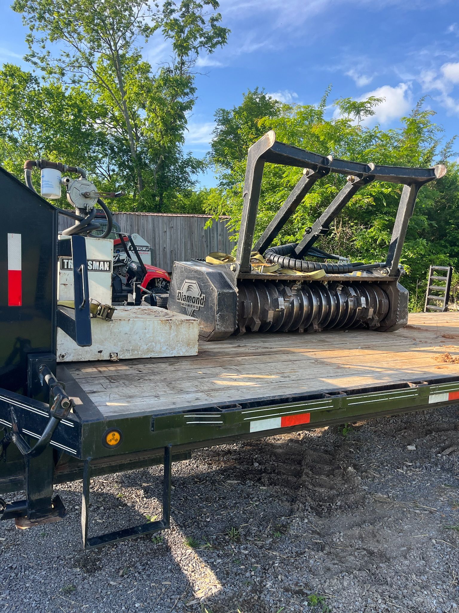 A trailer with a tractor on it is parked in a gravel lot.