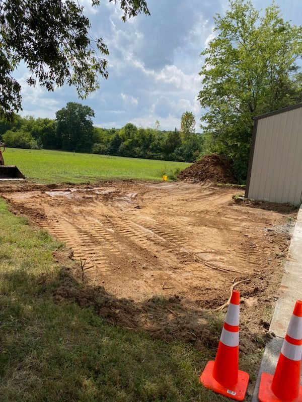Two orange and white traffic cones are sitting on the side of a dirt road.