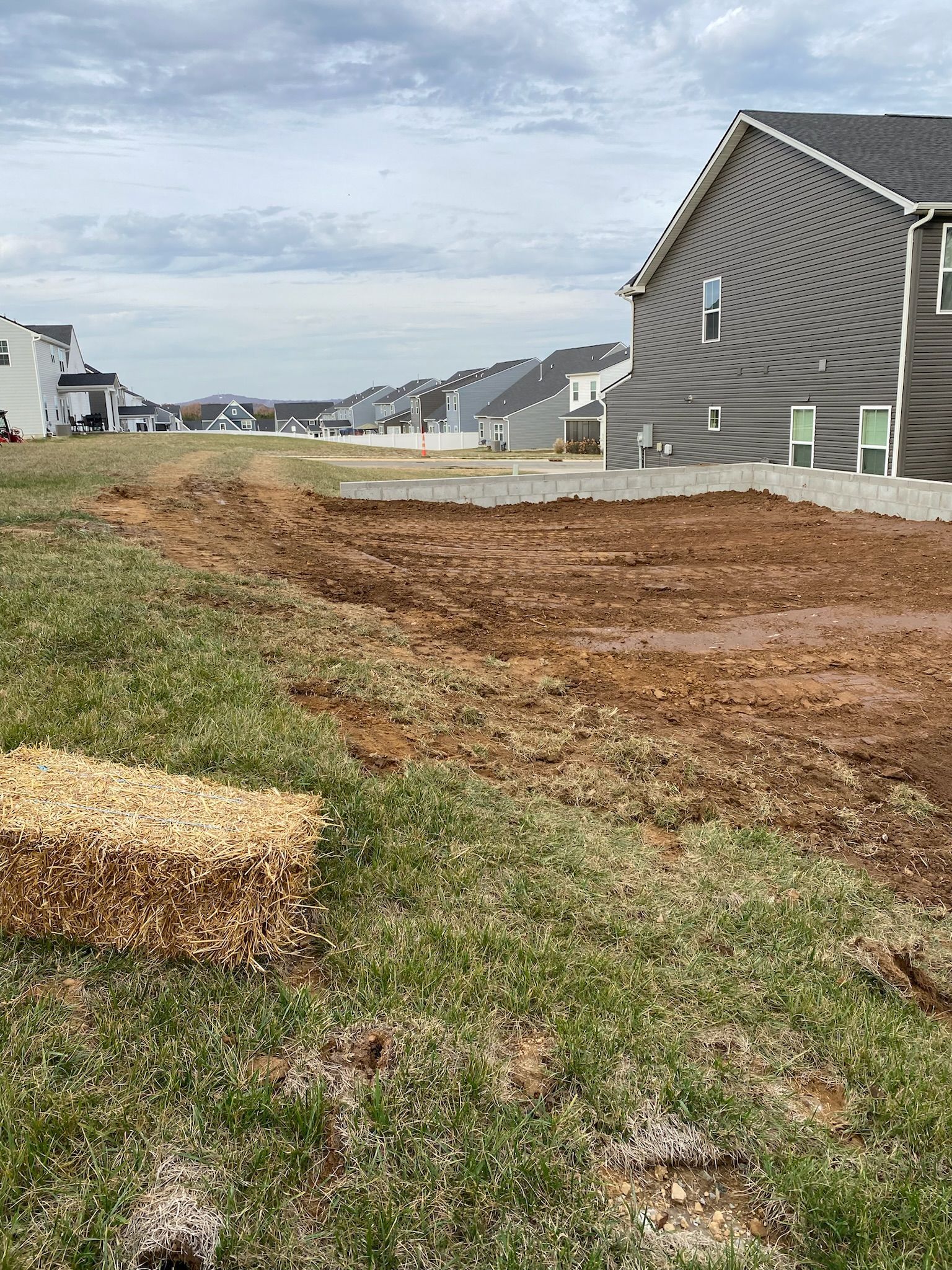 A pile of hay is sitting in the middle of a grassy field next to a house.