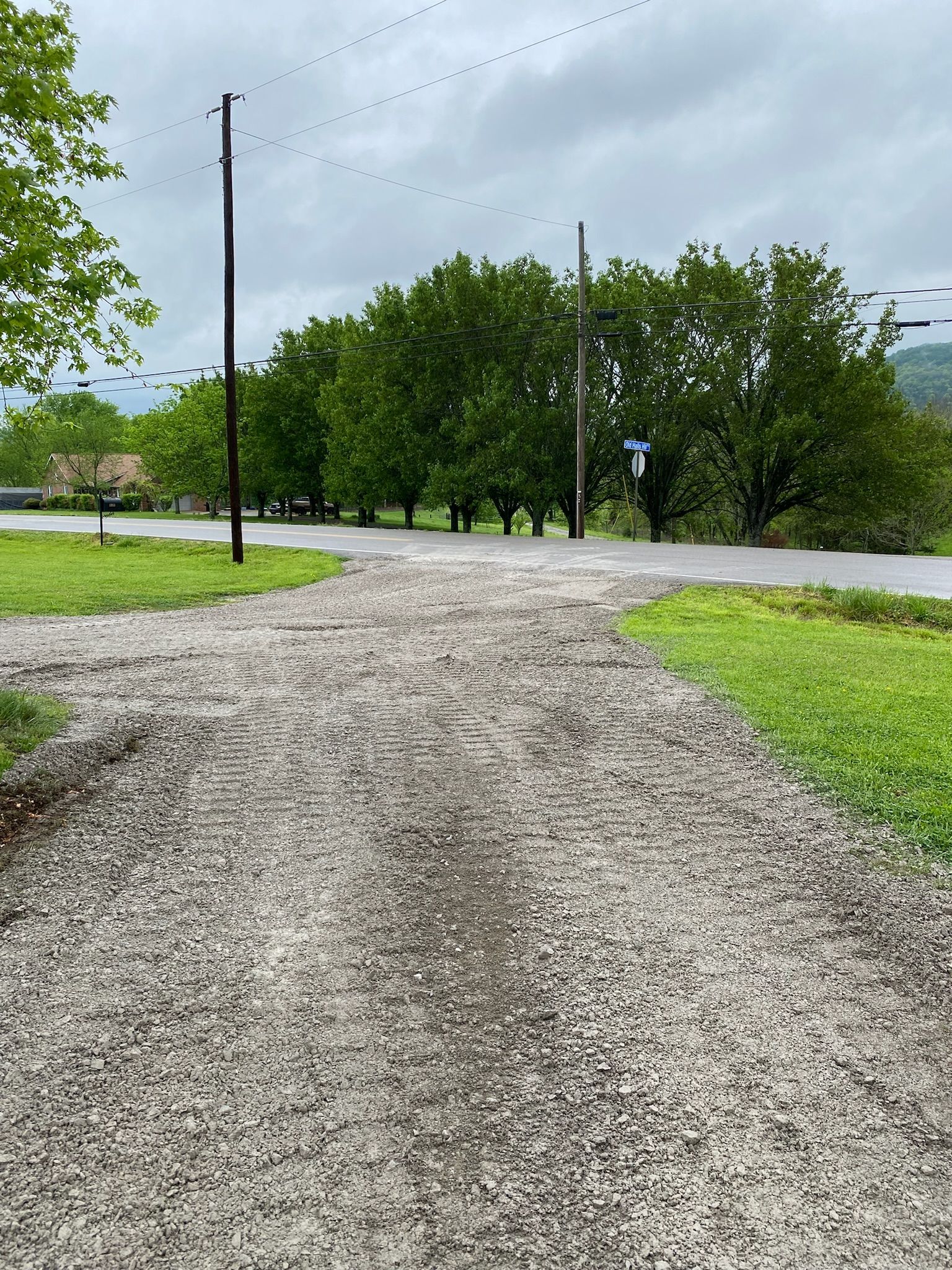 A gravel road going through a grassy field next to a road.