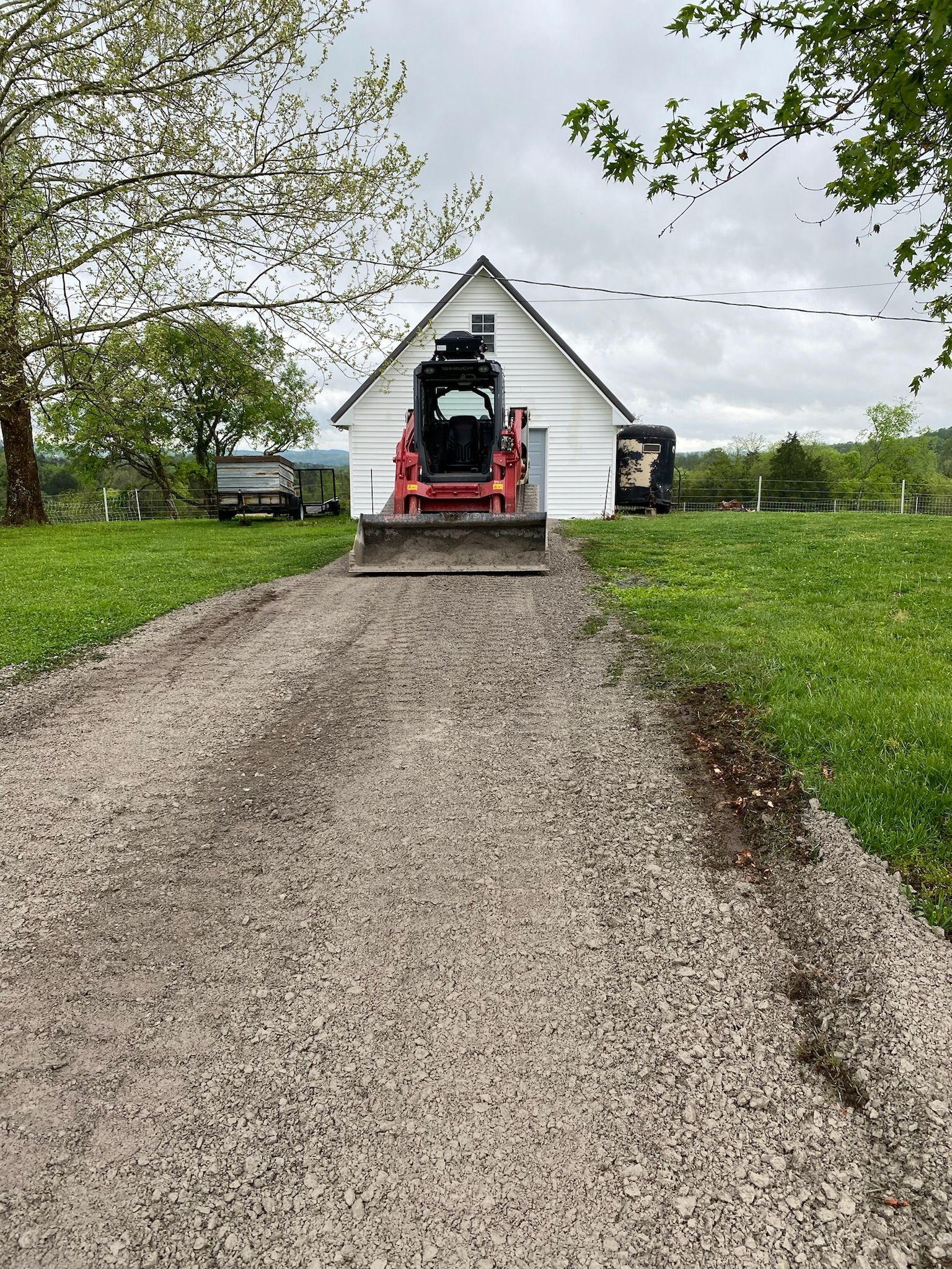 A bulldozer is driving down a gravel road in front of a house.