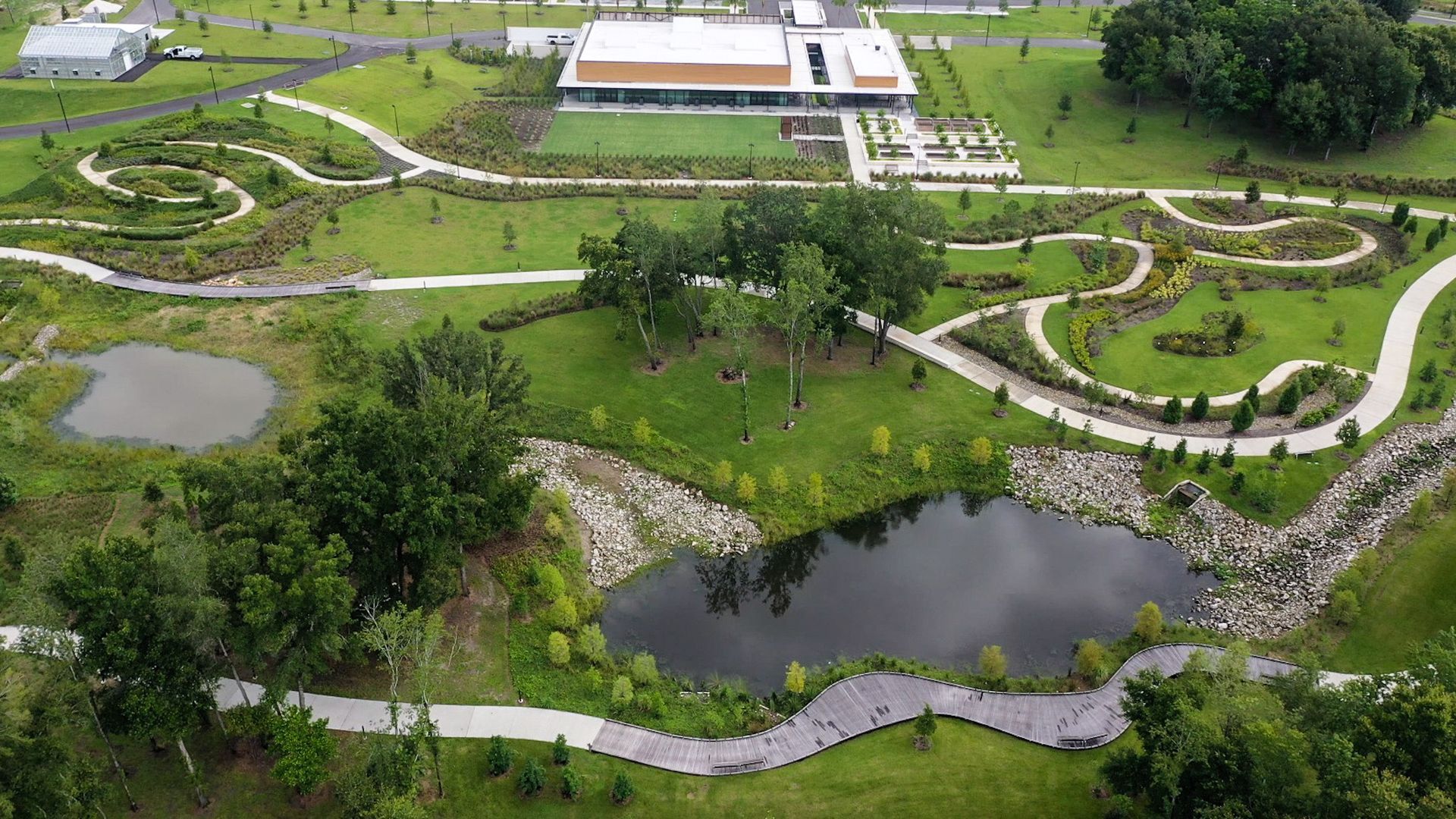 An aerial view of a park with a pond and a building in the background.