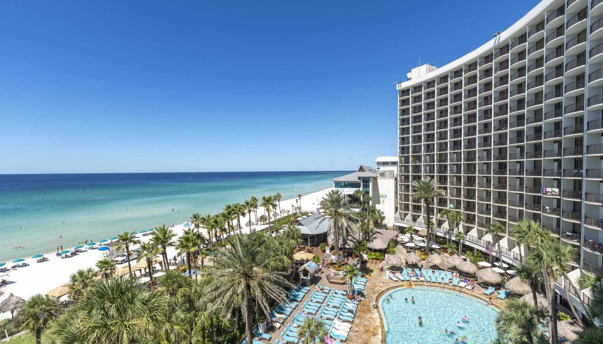 There is a large building with a pool in front of it and a beach in the background.