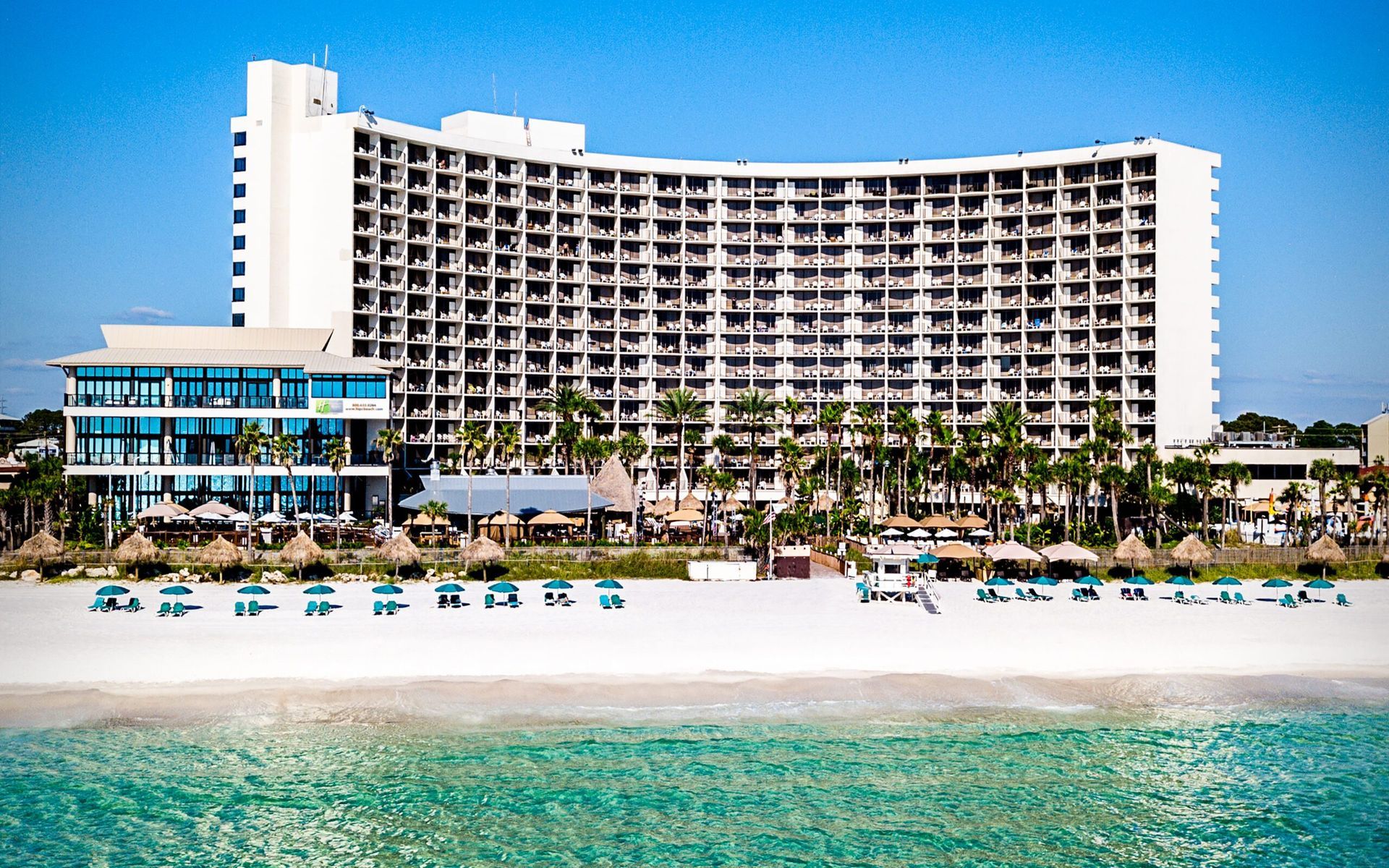 A large hotel is sitting on top of a sandy beach next to the ocean.