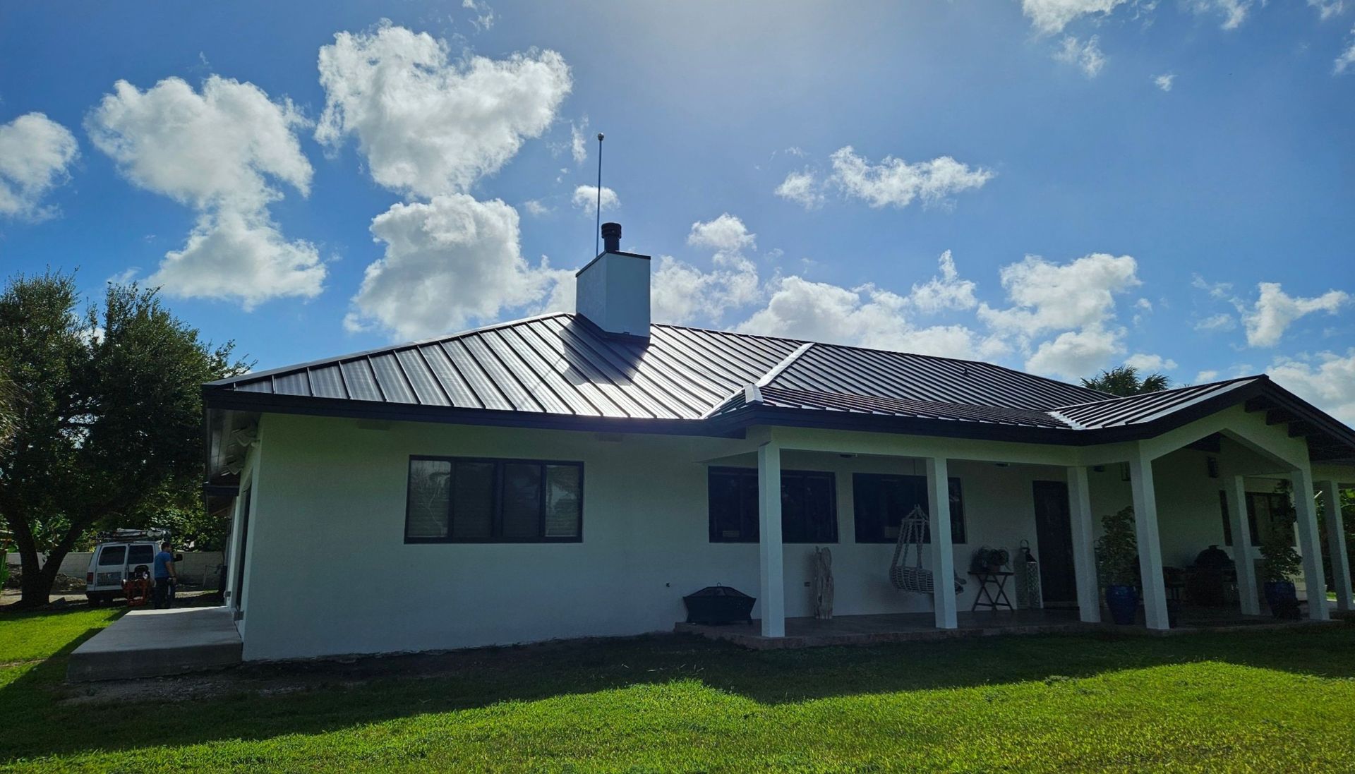 A white house with a black roof and a chimney on top of it.