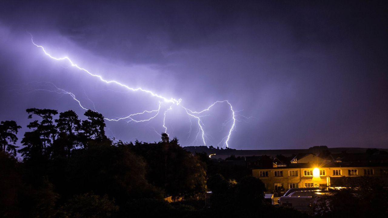 There is a lightning storm in the sky over a house.