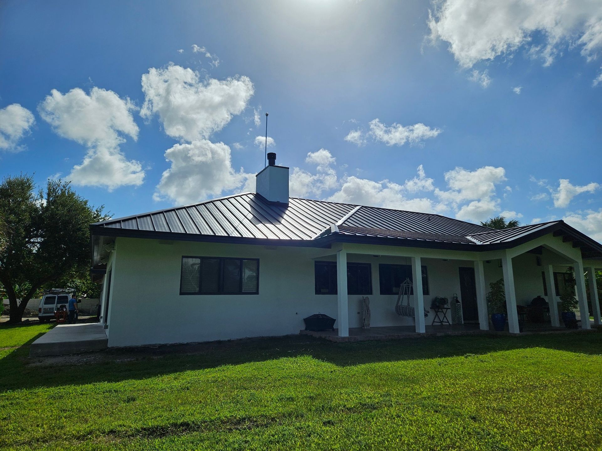 A white house with a black roof is sitting on top of a lush green field.