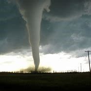 A tornado is moving through a field with a cloudy sky in the background.