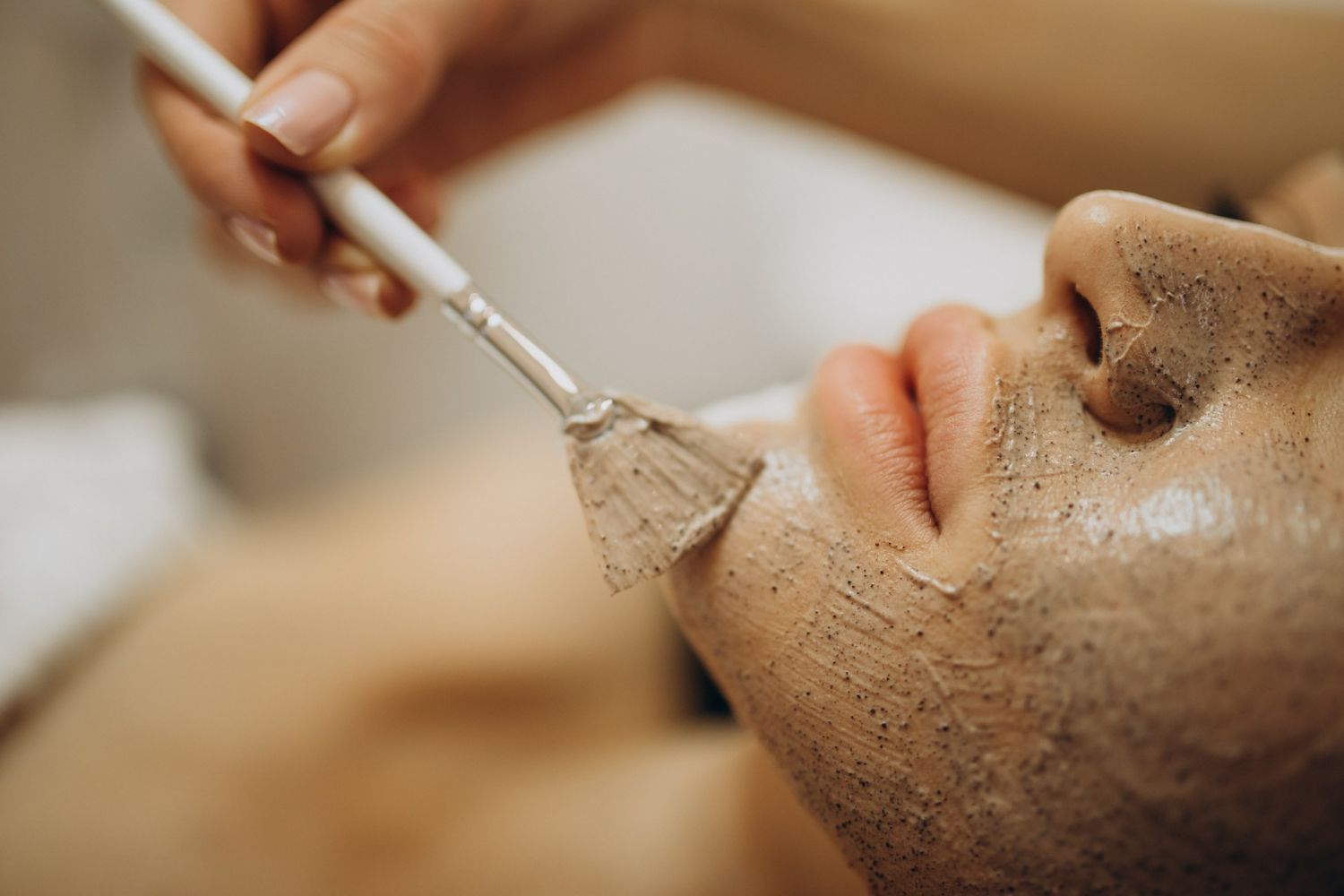 A woman is getting a facial treatment with a brush on her face.