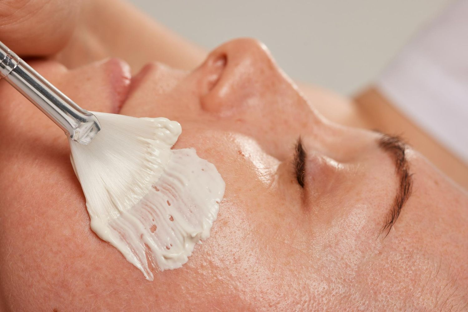 Facial treatment: Close-up of a person's face receiving a mask application with a brush.