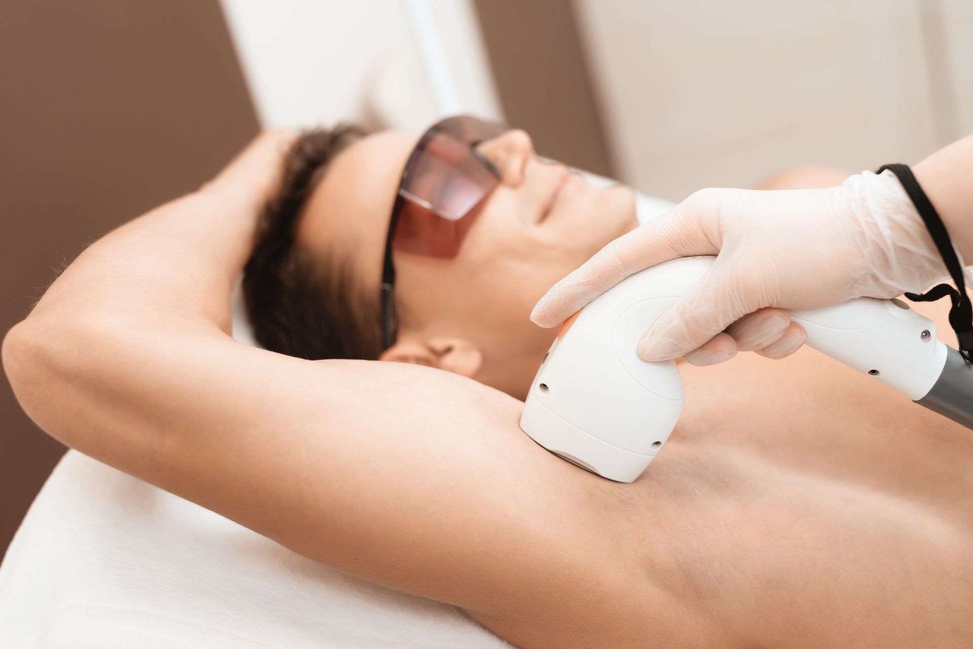 Close-up of a man lying down with his arm raised while receiving a laser hair removal treatment