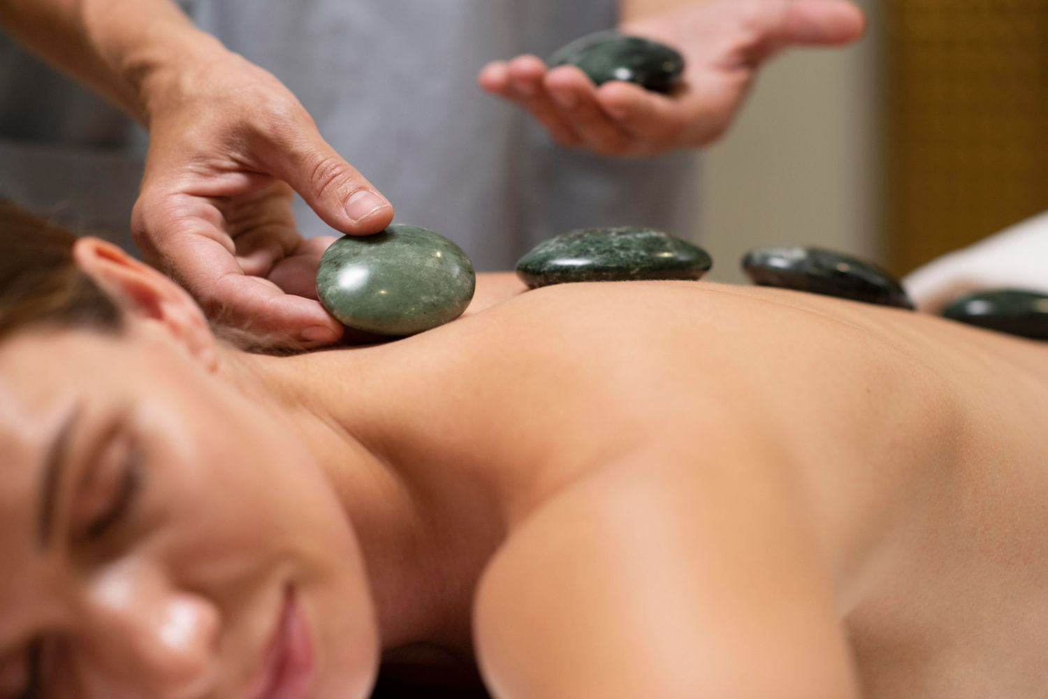 Person receiving a hot stone massage. Therapist placing stones on back, inside a spa.