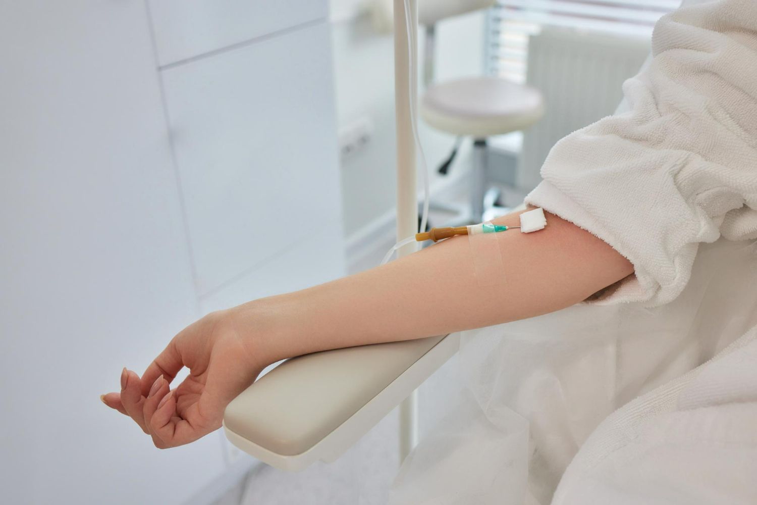 Person's arm with IV drip in a medical setting, wearing a white robe.