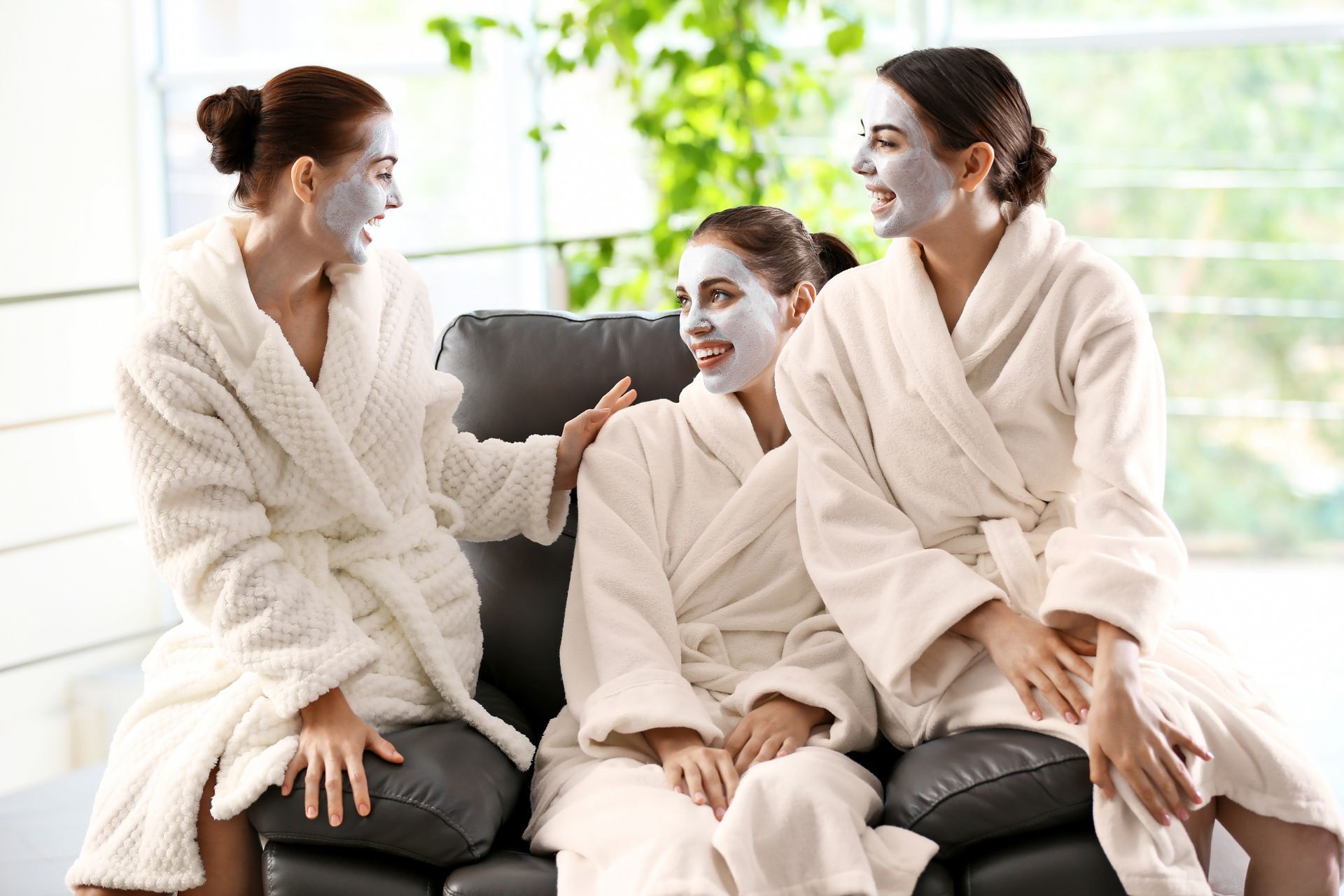 Three women in robes with face masks on a couch, talking.