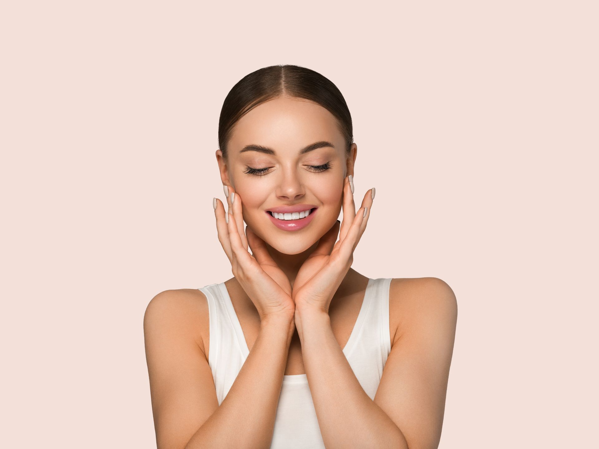 Woman with eyes closed, hands on cheeks, smiling. Light skin, tan background.