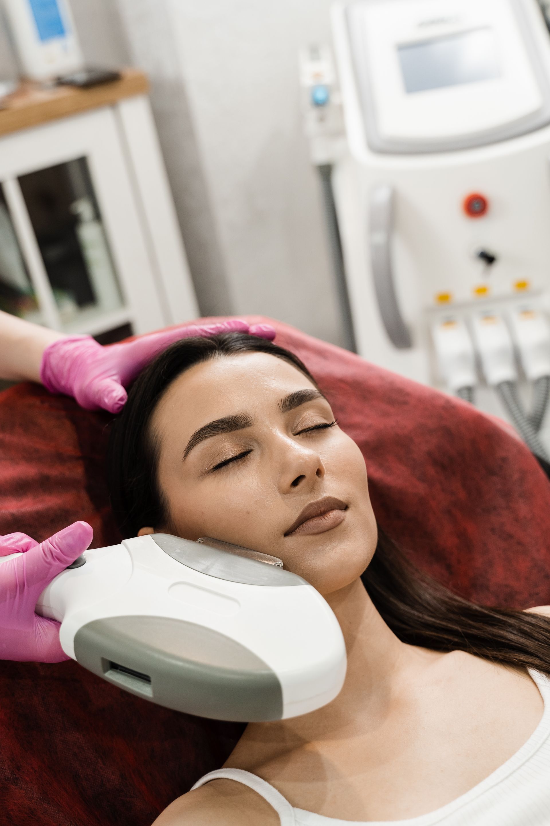 Woman receiving facial laser treatment in a clinic.  Technician in pink gloves holds a device to her face.