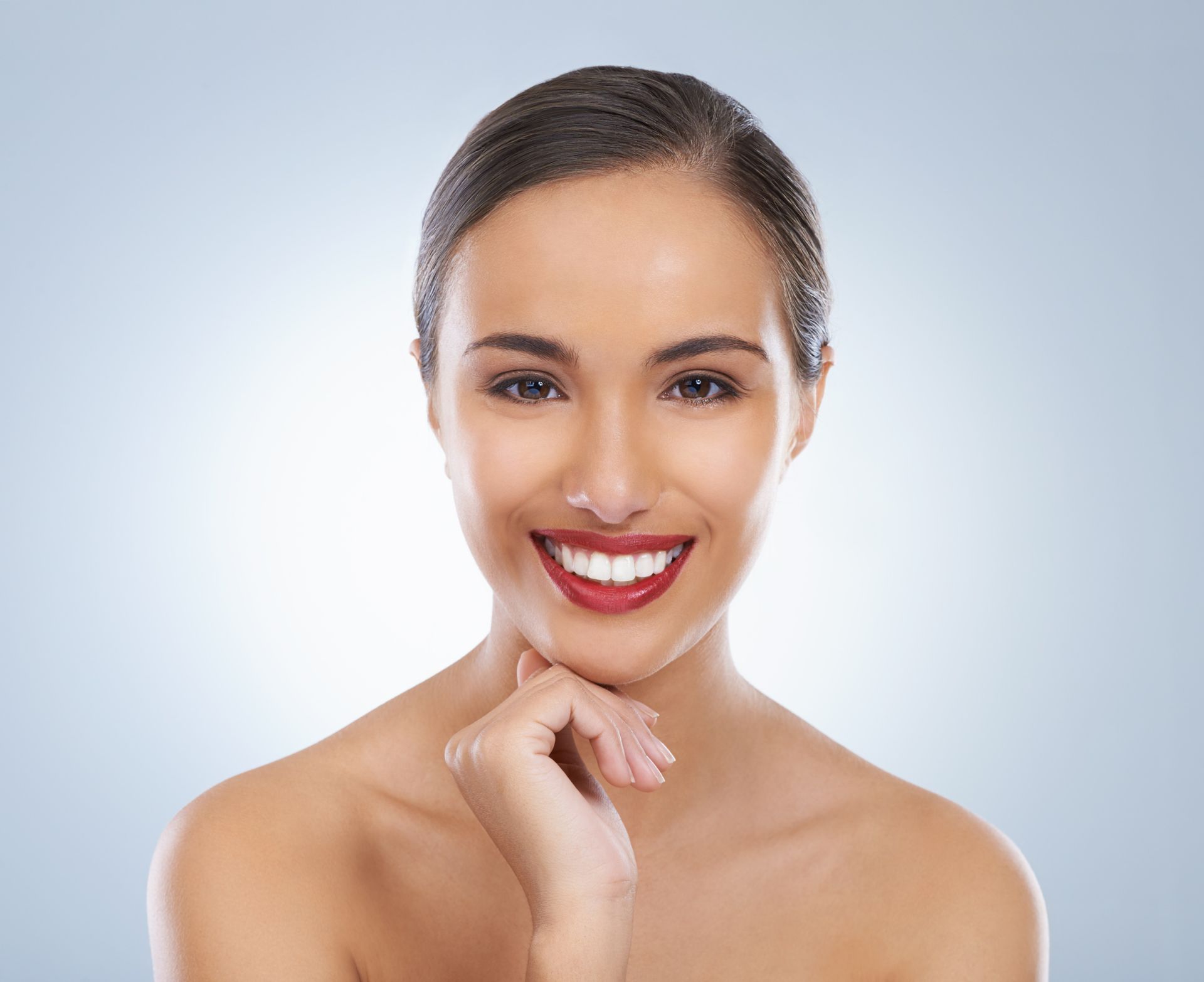 A woman with red lipstick is smiling and touching her face.