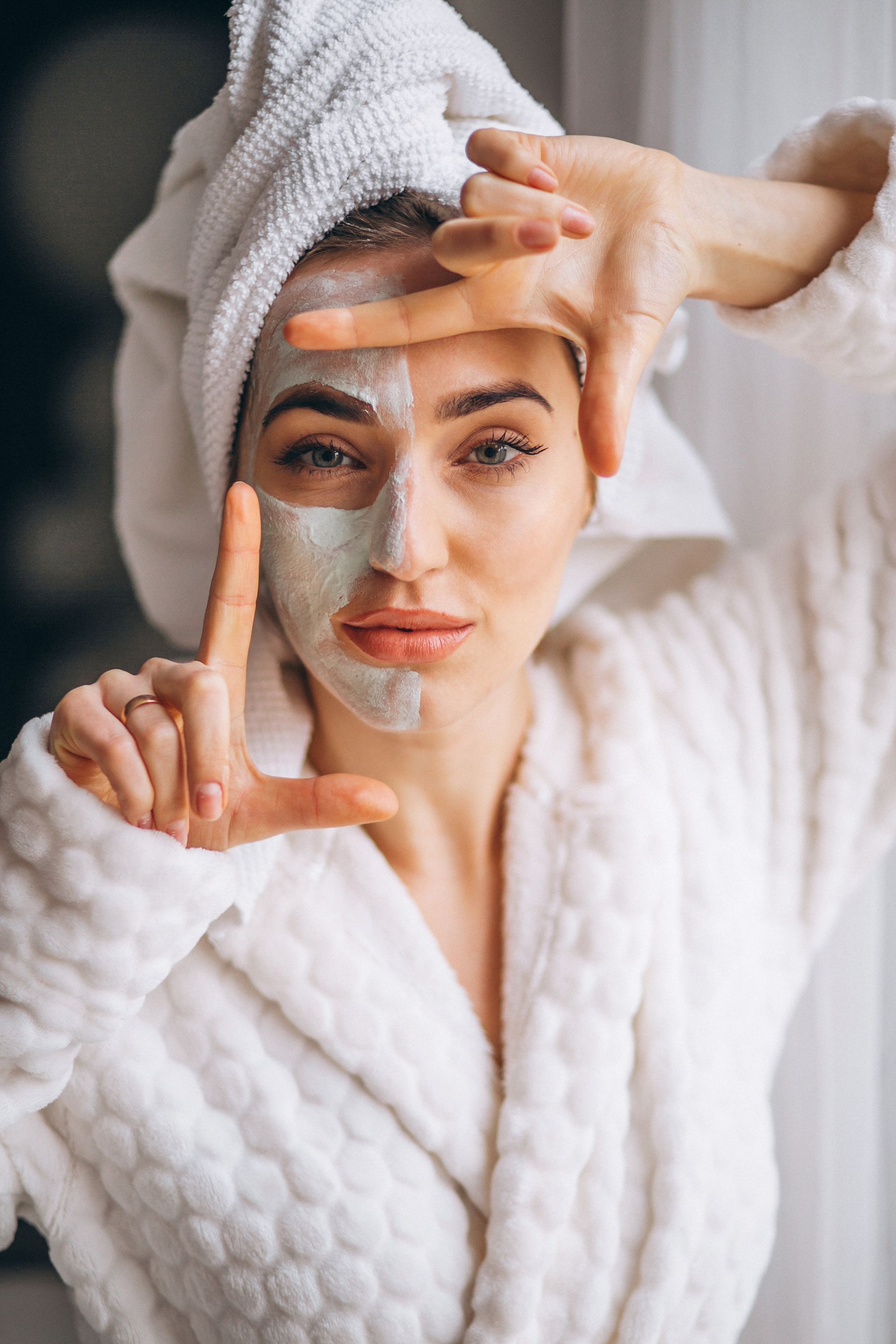 A woman with a mask on her face is making a frame with her hands.