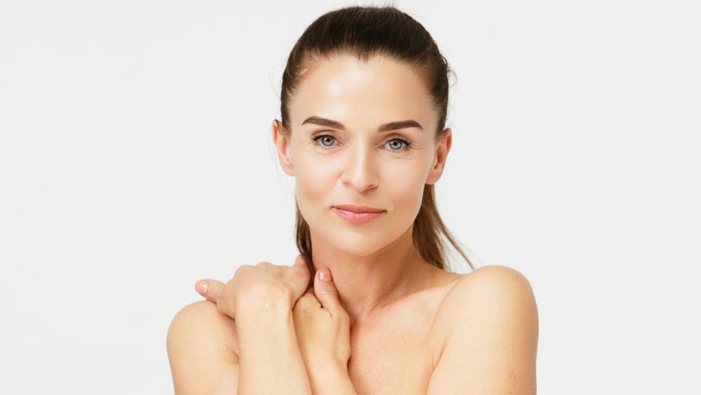 A woman without a shirt is holding her shoulder and looking at the camera.