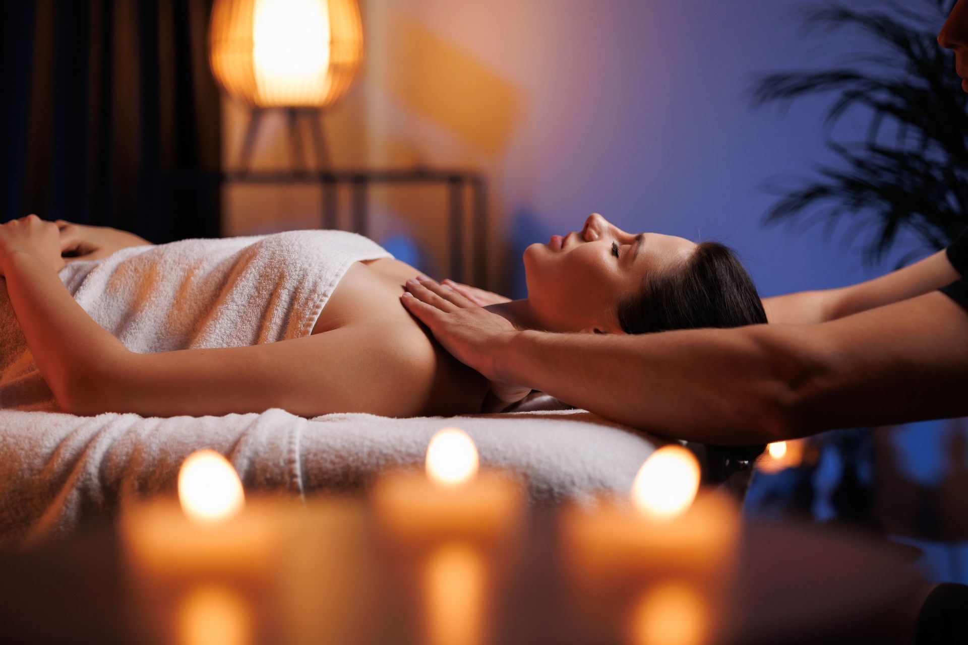 A woman is getting a massage at a spa with candles in the background.