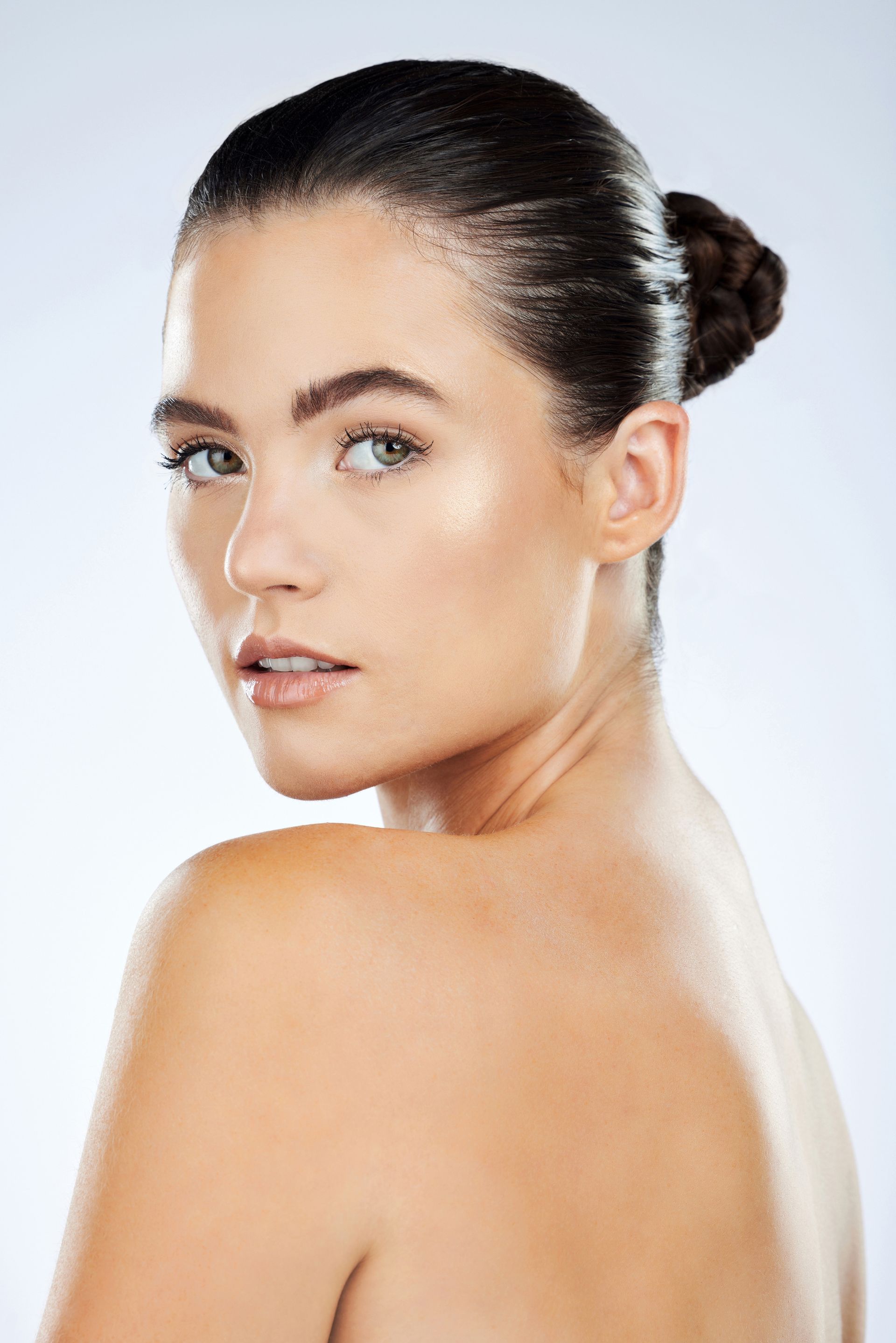 A woman with her hair in a bun is looking over her shoulder at the camera.