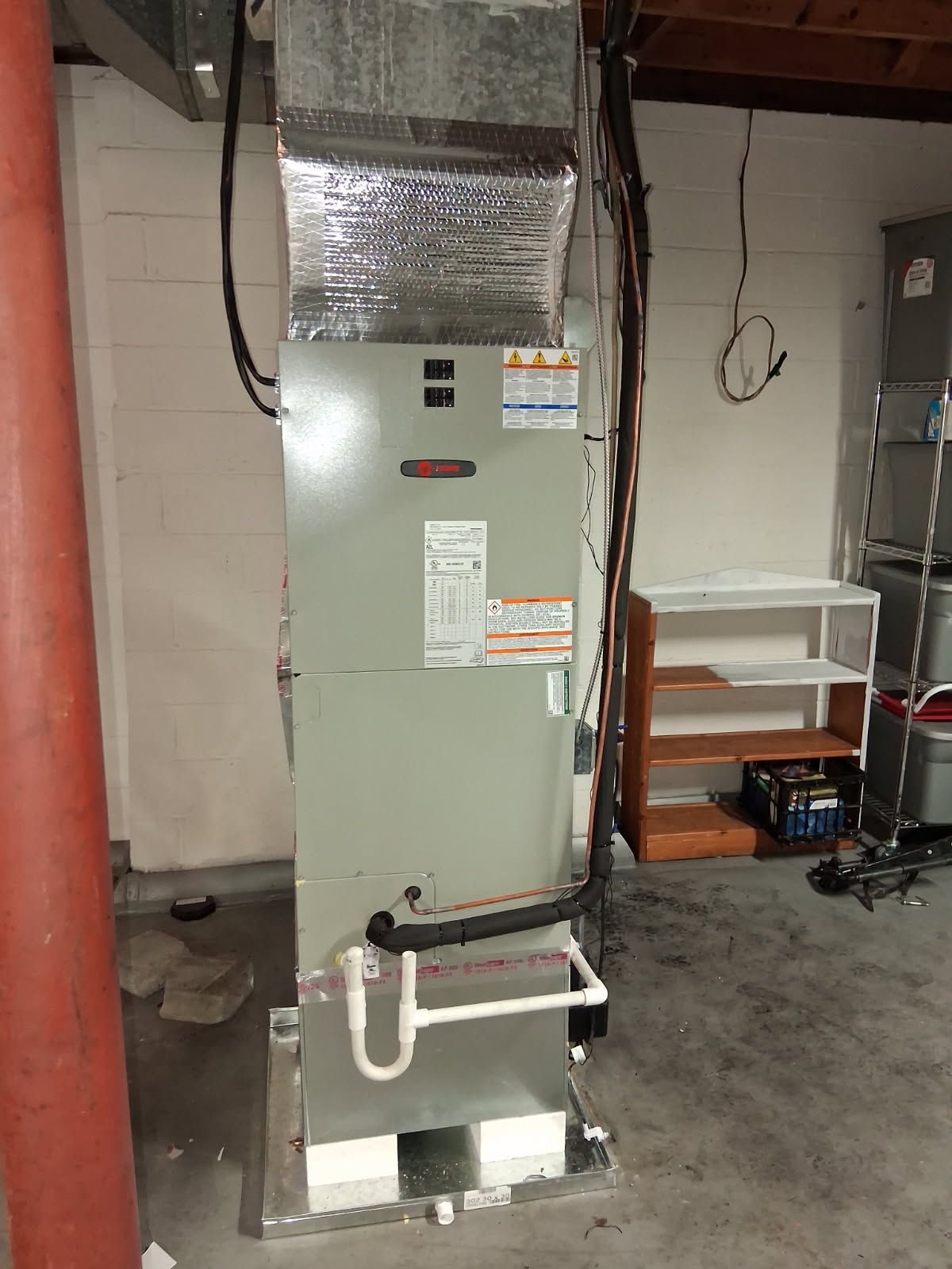 HVAC unit in a basement. Rectangular gray metal unit with ductwork, piping, and wiring.