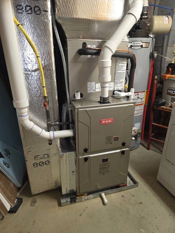 Furnace unit in a basement, with silver metal housing and white pipes.