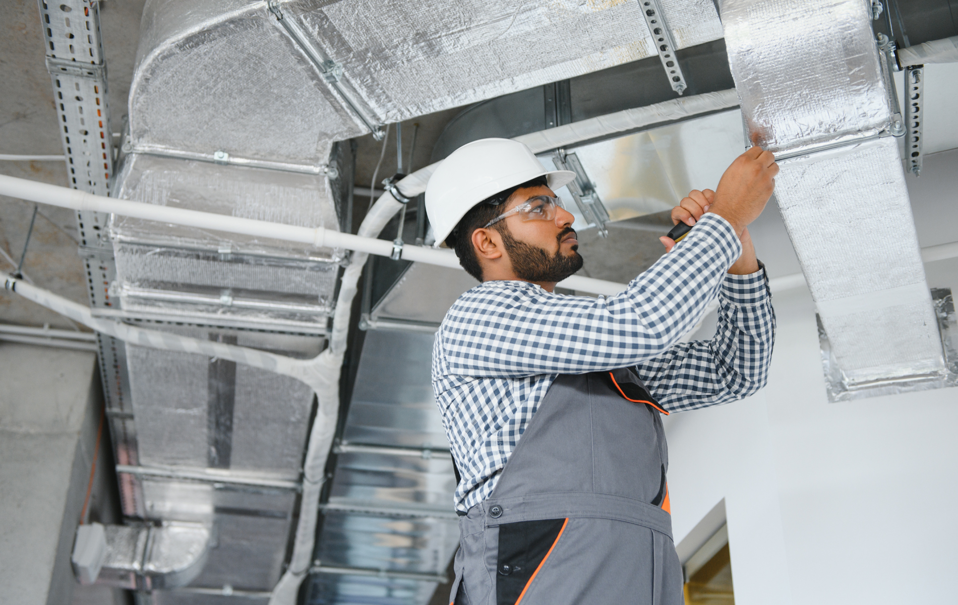 HVAC technician in a hard hat working on insulated ductwork in a building.