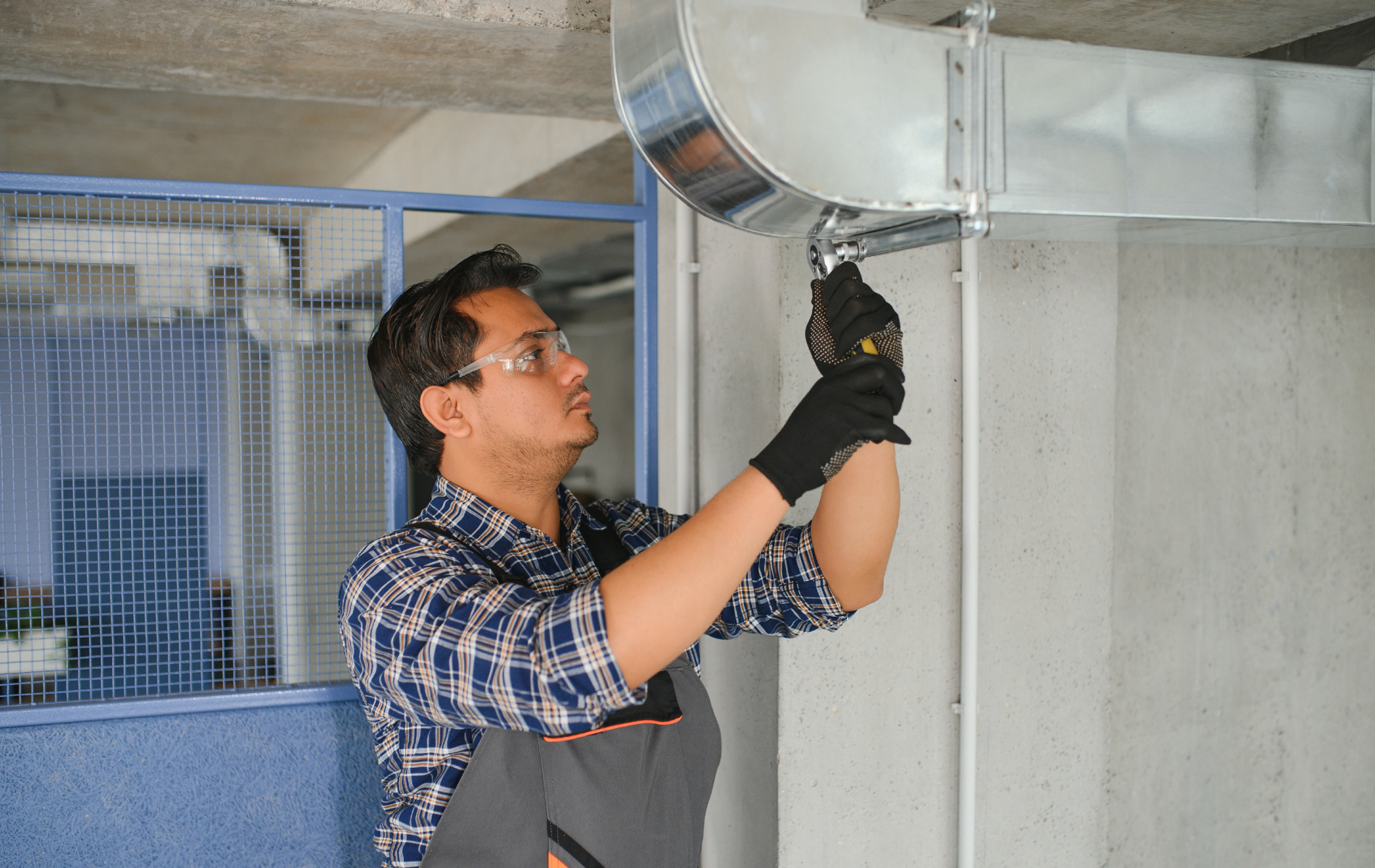 Man in safety glasses and gloves installing ductwork on a ceiling.